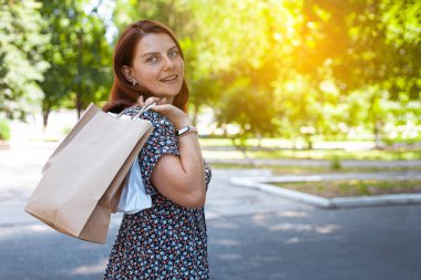 Güneşli bir günde, güneş gözlüklü, alışveriş torbalarıyla parkta gülümseyen güzel bir kız. Alışveriş konsepti