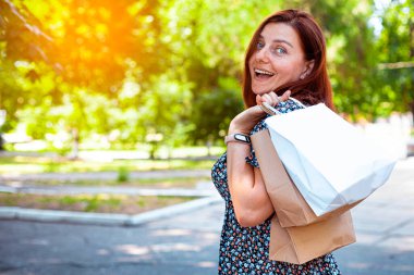 Güneşli bir günde, güneş gözlüklü, alışveriş torbalarıyla parkta gülümseyen güzel kız. Alışveriş konsepti
