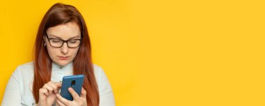 Gözlüklü ve mavi gömlekli kadın asistanı akıllı telefon kullanır ve sarı arkaplanda ayakta durmayı planlar