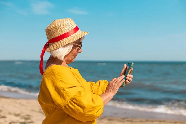 En vacker ung kvinna tar en selfie på stranden. Porträtt av en glad ung kvinna som ler mot havet — Stockfoto