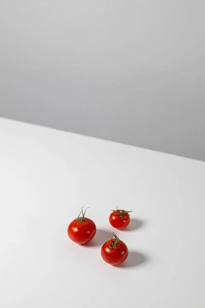 Trzy dojrzałe pomidory wiśniowe na białym stole, orientacja pionowa. Minimalny skład kreatywny — Zdjęcie stockowe