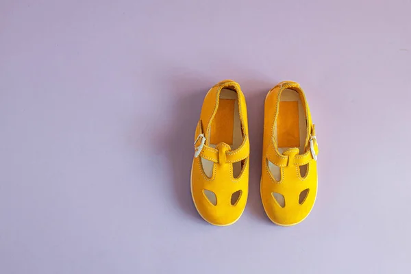 Sapatos de bebê amarelo brilhante em fundo lilás com copyspace. Conceito de roupas de bebê. — Fotografia de Stock