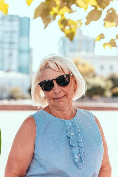 Портрет блондинки позитивно задоволеної зрілої жінки в сонцезахисних окулярах посміхається на камеру на відкритому повітрі в парку — стокове фото