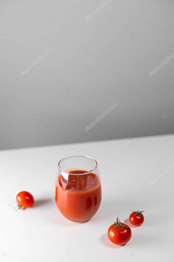 Vertical orientation photoshop of a glass of tomato juice and a lot of cherry tomatoes scattered on the table