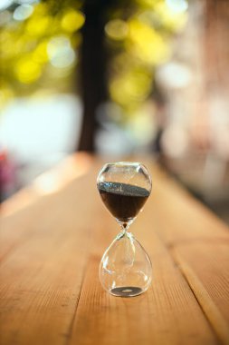 Dışarıda, güneş ışığının altında, ahşap masanın üzerinde kum saati. Son teslim tarihi konsepti. Dikey fotoğraf yönelimi