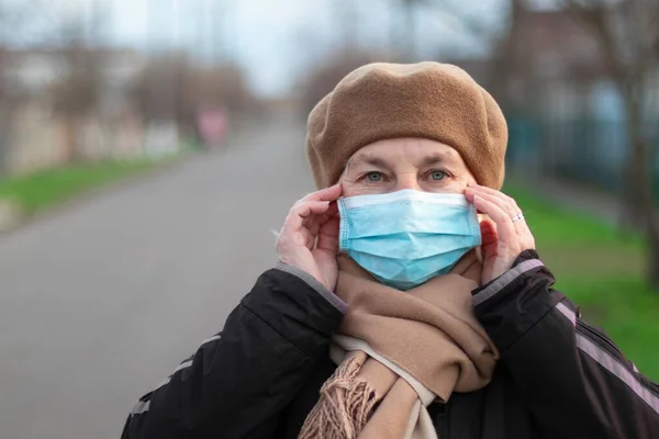 Portrait of an adult 40 50 years old woman in a medical mask and warm clothes looking at the camera, outdoors. Protection against contagious disease, coronavirus
