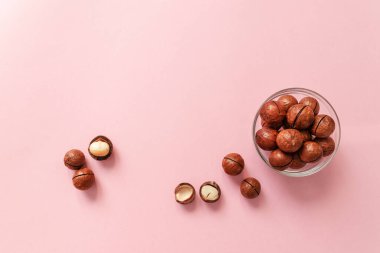 Şeffaf cam bir kasede çiğ macadamia fındığı ve pembe katı arka plana saçılmış. En düşük bileşim.
