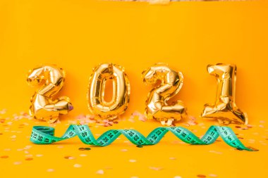 Yeni yıl 2021 folyo balonları sarı arka planda. Sarı arkaplanda yeşil mezura