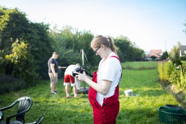Kırmızı önlüklü hamile bir kadın bahçede dikiliyor ve elinde fotoğraf makinesi, ekrandaki resimlere bakıyor. Annelik yaşam tarzı, hamilelik süresince hobiler ve aile eğlencesi kavramı. Beklentinin sembolü