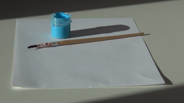 Papel, pincel y un frasco de pintura gouache de acrílico azul en la tabla — Vídeos de Stock