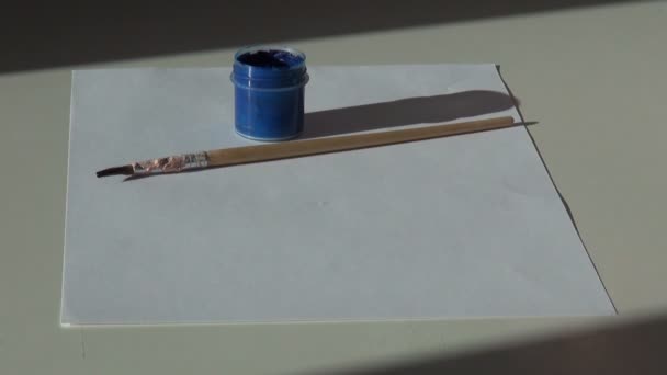 Χαρτί, βούρτσα και ένα βάζο με μπλε γκουάς ακρυλικό χρώμα για το tabl — Αρχείο Βίντεο