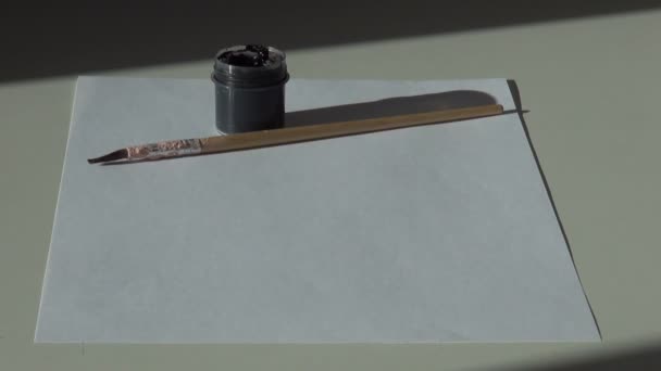 papier, pinceau et un pot de peinture à la gouache acrylique noire sur la languette 