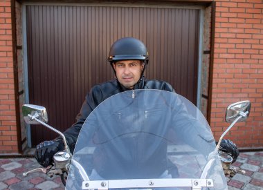 Motosikletli bir adam kasklı ve siyah ceketli.