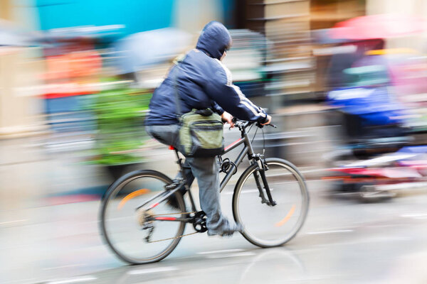 picture with camera made motion blur effect of a person with rain cape riding a bicycle