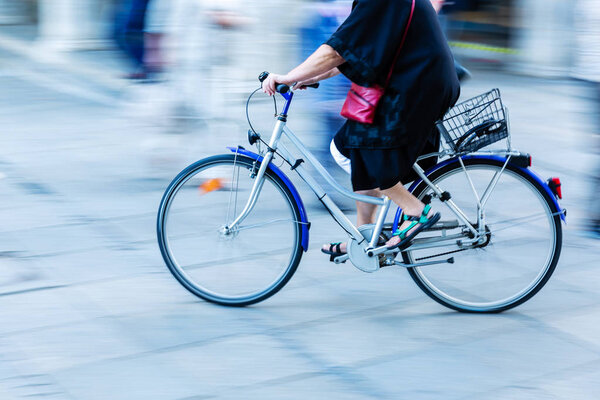 older woman rides a bicycle in the city with motion blur