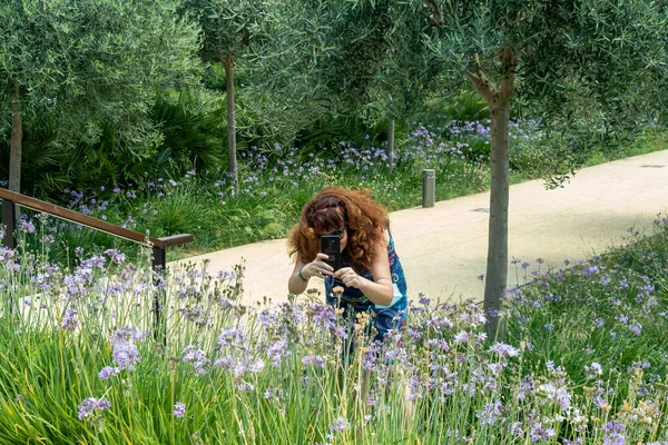 Femeia cu părul roșu în rochie cu flori în parc printre flori — Fotografie, imagine de stoc