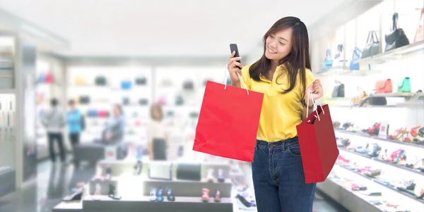 新しい通常のデジタルライフスタイルでスマートフォンで購入する前にオンラインチェック価格 幸せなアジアの女の子ファッションショップでの紙のショッピングバッグでの相対注文 バナーサイズとクリッピングパスを含む — ストック写真