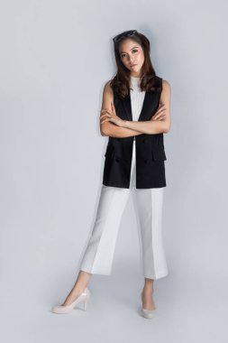 Zeki Asyalı kadın, beyaz arka planda iş elbisesiyle ayakta duruyor ve çapraz silah kullanıyor.