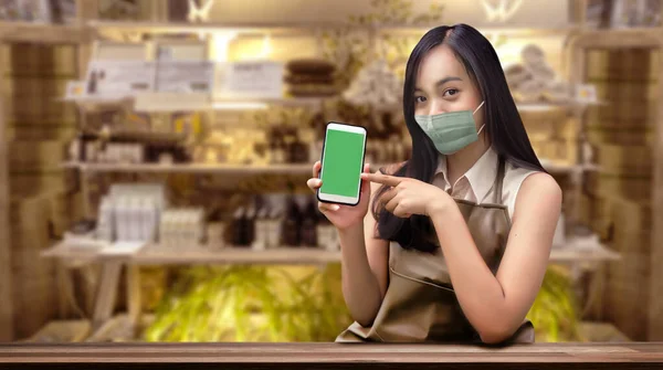 start online business with mobile to get order from customer and delivery in coronavirus pandemic. Asian woman show application mobile to deal business and wearing mask for protect virus.