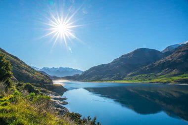 Wanaka Gölü kıyısında güneşli güzel bir günde bulutsuz gökyüzünde parlayan bir güneş.