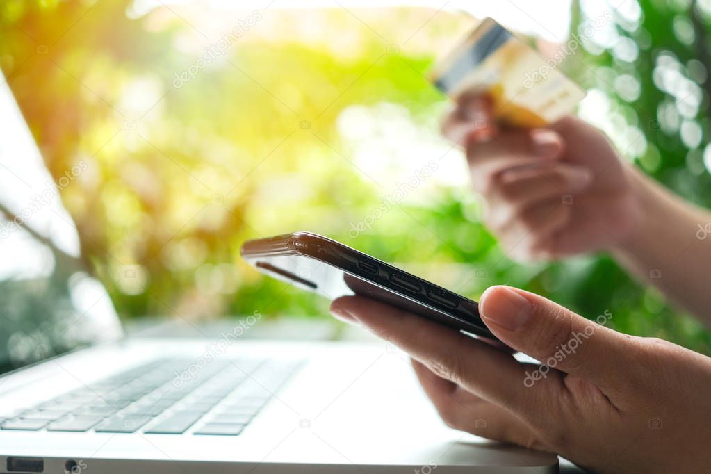 close up woman hand holding credit card, using smartphone outdoor for online shopping while working on laptop