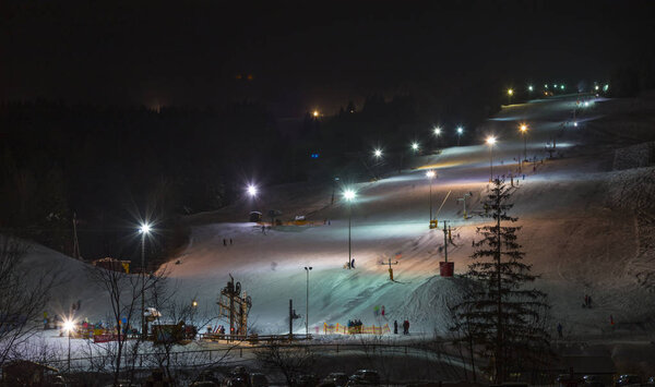 Night skiing. Zuberec Ski Park. Slovakia. Western Tatras. Europe. Ski slope with the lift at night lit by lanterns. Adults and children skiing. Tourist destination, winter holiday