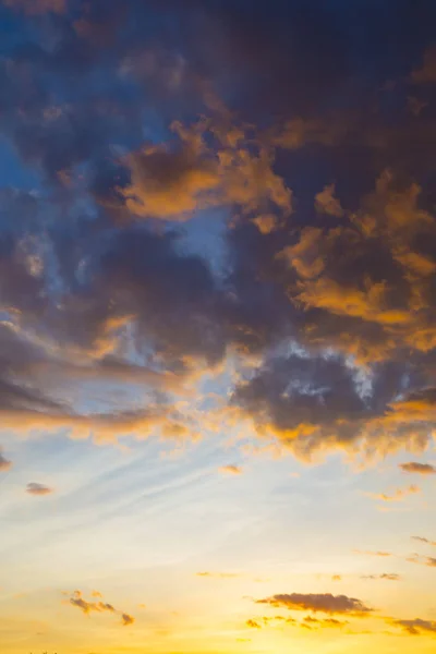 Blue sky with gold and orange clouds - dramatic sunset, beautiful natural background. Setting sun illuminates the clouds.