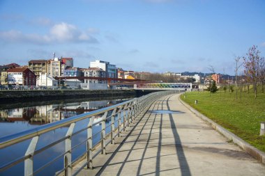 Metal parmaklıklı bir parkın fotoğrafı, birkaç bina, soğuk renkler ve güneş ışığı..