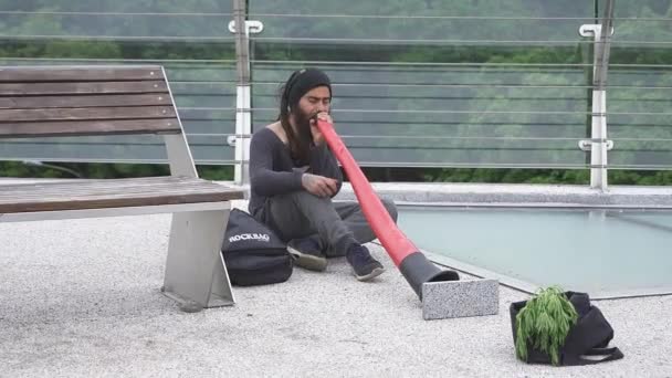 Músico callejero tocando en didgeridoo en puente a pie a través de la calle con lados de vidrio. Mayo 2020. Kiev, Ucrania. Prores 422 — Vídeos de Stock