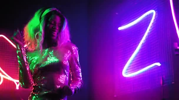 A lány egyedül táncol a füstgéppel. Afrikai amerikai lány táncol egy klubban neon elvont figura világítás egy ezüst fényes ruhát. Neon koncepció. Gyümölcsfélék — Stock videók