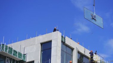 Vinç asılmış camları kaldırıyor, binanın tepesindeki inşaat işçileri zarar görmemesi ve zarar görmemesi için halat rehberini kullanarak binanın üst katına yerleştiriyor. Nisan 2020. Kiev, Ukrayna. Prores 422
