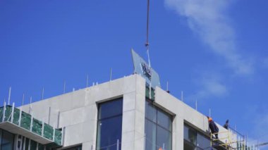 İnşaatçılar vinç rehberinin kaldırdığı camı tutarak zarar vermeden dengeleyip en üst kata yerleştirmeye yardım ediyorlar. Nisan 2020. Kiev, Ukrayna. Prores 422