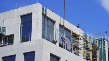 İnşaatçılar, en üst kata yerleştirmek için vinç tarafından kaldırılan büyük bir camı tutup açıyorlar. Nisan 2020. Kiev, Ukrayna. Prores 422