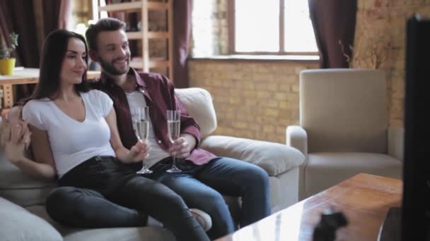 Una pareja celebra el aniversario bebiendo champán mientras se sienta en un sofá en el pasillo frente al televisor viendo el día de su boda. Concepto familiar. Prores 422 — Vídeos de Stock