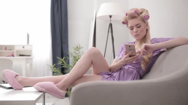ソーシャルネットワークやオンラインストアを介してブロンドの親指カーラーでカール髪に座っている。彼女自身が隔離で髪の世話をしている。家のコンセプトを維持。第四百二十二条 — ストック動画