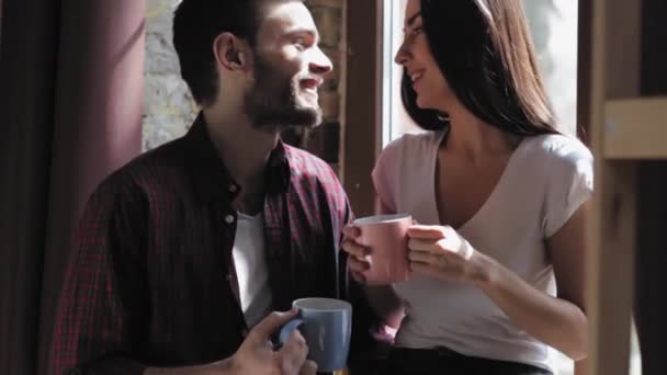 Szerető pár iszik reggeli kávét, miközben áll az ablak előtt készül dolgozni, és megbeszéljük a terveket. A feleség az ablakpárkányon ül egy kávéval, miközben egy szerető férj áll a közelben. Gyümölcsfélék — Stock videók