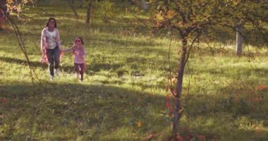 Anne ve kızı sonbahar parkında renkli bir peri masalı renginde ağaçların arasında el ele tutuşarak maymun atlayışı yapıyorlar. Renkli görüntüler. Uzayı kopyala Aile kavramı. Prores 422