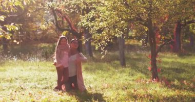 Anne dizlerinin üzerine çöküp kızına sarılıyor sonbahar parkında ağaçların arasında onu ne kadar çok sevdiğini anlatıyor renkli bir peri masalı renginde. Uzayı kopyala Aile kavramı. Renkli görüntüler. Prores 422