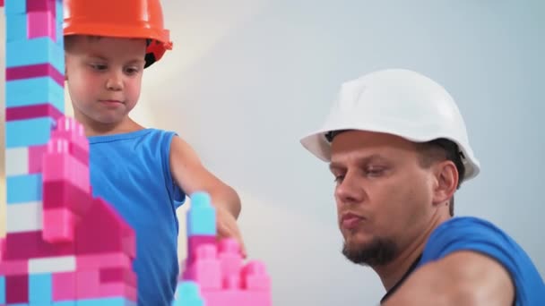 父亲和他的儿子戴着建筑用的钢盔打砖头，帮助他展示如何正确建造城堡。2019.June Kiev, Ukraine.Prores 422 — 图库视频影像