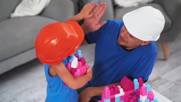 建筑工人的父亲和他的儿子戴着建筑用钢盔玩砖头，帮助他展示如何建造城堡。父子关系的概念。2019.June Kiev, Ukraine.Prores 422 — 图库视频影像