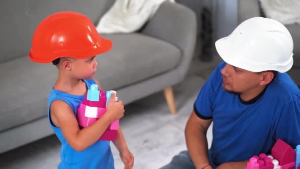 给爸爸的儿子5岁的儿子建筑工人戴着建筑用的钢盔玩砖头，打开相机笑了。父子关系的概念。2019.June Kiev, Ukraine.Prores 422 — 图库视频影像