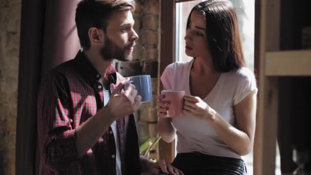 Café du matin au couple amoureux du matin lumineux debout par la fenêtre se préparant à travailler et discuter des plans. Femme est assise sur le rebord de la fenêtre avec un sourire de café et donnant mari un baiser. Prores 422 — Video