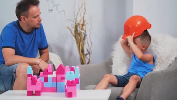 Father telling his son how to wear construction helmet playing brick constructor building castles. Father and son concept. June 2019.Kiev, Ukraine. Prores 422 — Stock Video