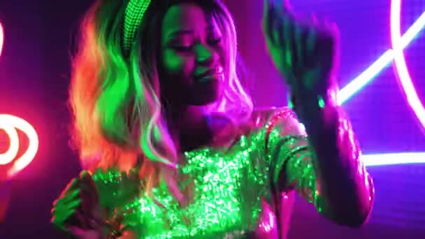 Joyeux mannequin féminin dansant aux néons à la caméra. Fille africaine dansant sur néon figure abstraite éclairage dans une robe brillante argentée. Concept néon. Prores 422 — Video