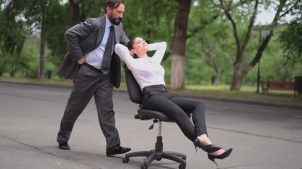 Bir adam, çalışanlarıyla alay ettiği bir kadın patronun olduğu bir sandalyeyi sokağa itiyor. Kız çalışanların kendisini eğlendirmesini sağlıyor. İş yerinde taciz. Prores 422 — Stok video