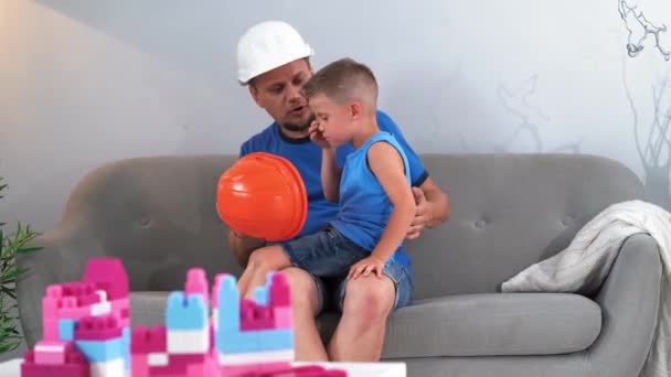 Padre se pone cascos de construcción en la cabeza hijos explicando lo que es para mientras juega constructor de ladrillo. Concepto de padre e hijo. Junio 2019.Kiev, Ucrania. Prores 422 — Vídeos de Stock