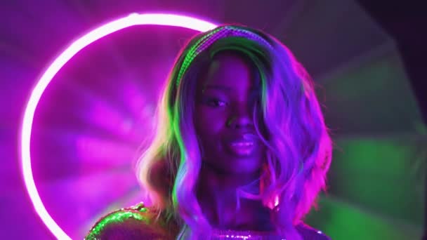 Modello sensuale posa in luci al neon ballare sulla macchina fotografica. Ragazza afroamericana che balla in studio fotografico in figura astratta al neon illuminata da un abito argentato brillante. Concetto al neon. Prore 422 — Video Stock