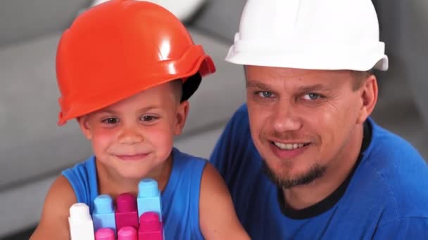 爸爸和儿子看着摄像机，和一个在建筑行业工作的儿子在玩建筑工人的砖头游戏。父子俩的概念Prores 422 — 图库视频影像