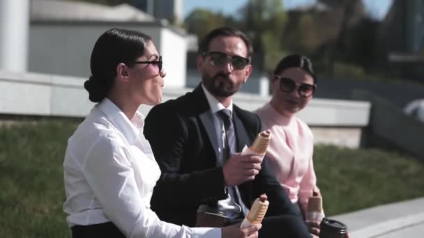 Gente de negocios comiendo perritos calientes en ropa de negocios y gafas de sol al aire libre cerca del edificio de oficinas. Gente de negocios almorzando comiendo en la calle. Comida saludable. Concepto de negocio. Prores 422 — Vídeo de stock