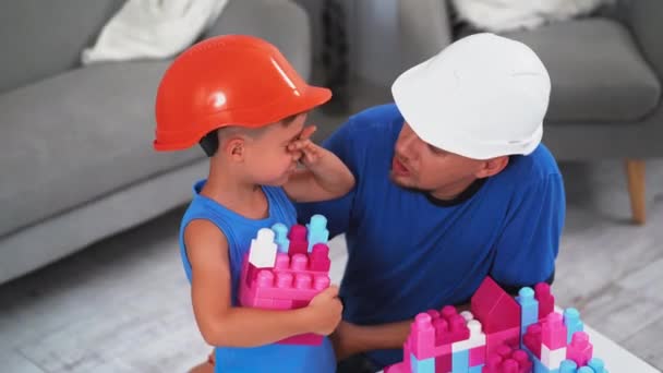 父亲让儿子平静下来，戴着建筑用的钢盔，手里拿着砖头，帮助他展示如何正确建造城堡。父子俩的概念Prores 422 — 图库视频影像